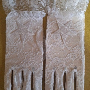 May include: A pair of white lace gloves with a star design on each glove. The gloves have a ruffled lace trim at the wrist.
