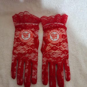 May include: A pair of red lace gloves with a scalloped edge at the wrist. Each glove features a circular emblem with the text "HEROINES OF JERICHO" and a graphic of a chair.