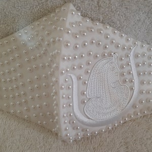 May include: White face mask with a white embroidered design of an Egyptian goddess and embellished with white pearls.