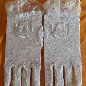 May include: A pair of white lace gloves with a floral design and a small embroidered design on the back of each glove.