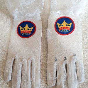 May include: A pair of white lace gloves with a red, blue, and yellow crown patch on each glove. The patch says "PYCH" underneath the crown.
