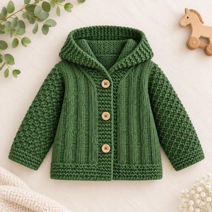 May include: A forest green hooded cardigan featuring a textured knit pattern on the sleeves and hood, with vertical cable knit detailing on the front panels. The garment is fastened with three light brown wooden buttons down the centre front.
