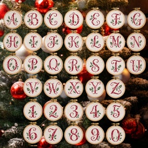 May include: A collection of circular wooden embroidery hoops containing cross-stitched letters and numbers in red thread, each accented with green holly leaf motifs on a white fabric background, arranged in a grid pattern.