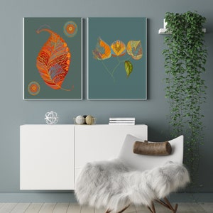 Puede incluir: Dos impresiones enmarcadas de hojas estilizadas de color naranja y amarillo sobre un fondo azul verdoso. Las impresiones est&aacute;n colgadas en una pared azul claro sobre un armario blanco y una silla mecedora blanca con un coj&iacute;n marr&oacute;n.