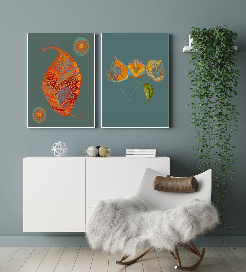 Puede incluir: Dos impresiones enmarcadas de hojas estilizadas de color naranja y amarillo sobre un fondo azul verdoso. Las impresiones est&aacute;n colgadas en una pared azul claro sobre un armario blanco y una silla mecedora blanca con un coj&iacute;n marr&oacute;n.