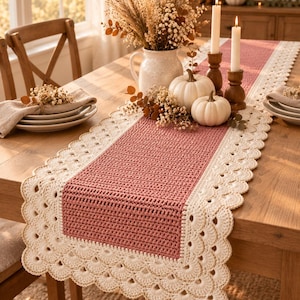 May include: A rectangular crochet table runner featuring a dusty rose center panel with a textured stitch pattern, bordered by a wide, cream-colored scalloped edge with delicate gold thread accents. The runner is displayed on a wooden table.
