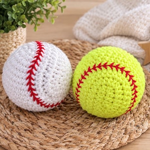 Könnte beinhalten: Zwei kugelförmige Häkelbälle, einer in Weiß und einer in Neongelb, jeweils mit einem markanten roten Nahtmuster, das wie bei einem Baseball und einem Softball aussieht. Diese handgefertigten Garnartikel sind rund und strukturiert.