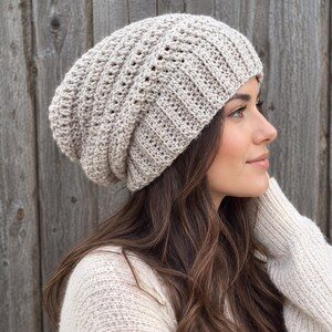May include: A light beige slouchy beanie hat featuring a textured crochet knit pattern with vertical ribbed detailing along the wide brim. The hat has a relaxed, oversized fit that sits comfortably on the head with a soft, woven appearance.
