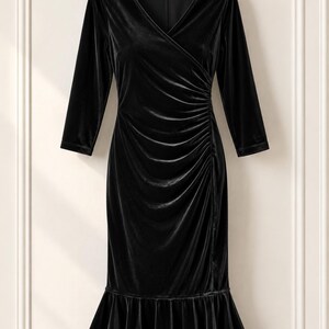May include: A black velvet dress featuring a V-neckline, three-quarter length sleeves, and a fitted bodice with side ruching. The skirt includes a flared ruffle hemline, creating a mermaid silhouette. The dress is displayed on a wooden hanger.
