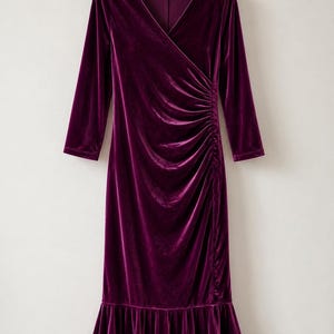May include: A deep purple velvet dress featuring a V-neckline, three-quarter length sleeves, and a side-ruched waist detail. The garment has a fitted bodice that transitions into a flared, ruffled hemline, hanging from a wooden hanger.