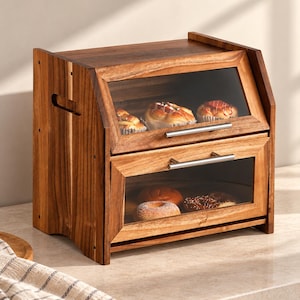 May include: A two-tier wooden bread box with a dark brown finish, featuring two hinged doors with clear glass panels and horizontal silver metal handles. The interior compartments contain various baked goods like rolls and donuts.