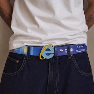 Könnte beinhalten: Ein blauer Gürtel mit einer Schnalle in Form des Internet Explorer-Logos. Der Riemen zeigt ein wiederkehrendes Muster aus Computersymbolen und den Text 3:39 AM 10/22/2009. Der Gürtel wird zu einem schlichten weißen T-Shirt und einer dunkelblauen Jeans getragen.