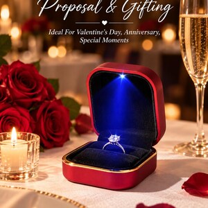 May include: A square red ring box with a gold-tone rim and a black velvet interior, featuring an integrated blue LED light that illuminates a silver-tone ring with a central stone. The box displays the text Perfect For Proposal & Gifting.
