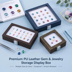 May include: Three rectangular and square jewelry display boxes with clear lids and metal latches. One box is dark blue, one is dark brown, and one has a black and gold patterned exterior. Each contains small colorful gemstones on a white base.