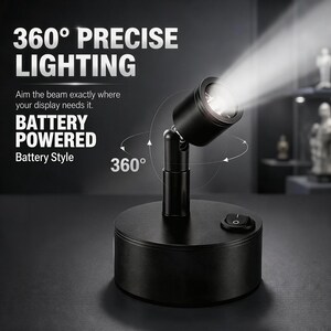 May include: A black battery-powered spotlight with a cylindrical head on a swivel mount and a circular base featuring an on-off switch. Text on the image reads 360 PRECISE LIGHTING, Aim the beam exactly where your display needs it, BATTERY POWERED, Battery Style, and 360.