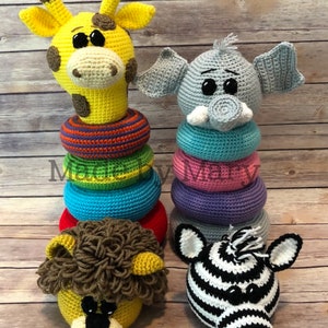Könnte beinhalten: Gehäkelte Tier-Stapeltürme. Eine gelbe Giraffe mit braunen Flecken und einem Regenbogen-Ringstapel. Ein grauer Elefant mit einem blauen, rosa und lila Ringstapel. Ein Löwen- und ein Zebra-Kopf.