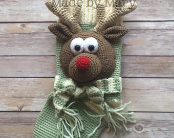May include: A green and white crocheted Christmas stocking with a reindeer face. The reindeer has brown fur, big eyes, a red nose, and antlers. The stocking has a white and green striped scarf with tassels.