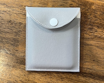 May include: A grey felt pouch with a white button closure. The pouch is ideal for storing small items like jewellery or electronics.