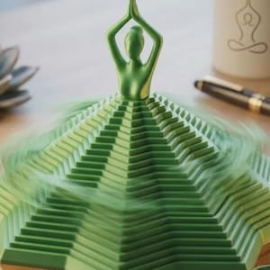 May include: A metallic green figurine of a person in a yoga pose with hands joined above the head. The figure is attached to a base composed of multiple stacked, tiered, hexagonal layers that create a wide, skirt-like structure with a smooth finish.