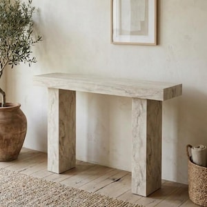 May include: A rectangular console table featuring a light beige stone-like finish with subtle grey veining. The piece has a thick, flat top supported by two wide, solid vertical legs, creating a clean, structured silhouette with a neutral appearance.