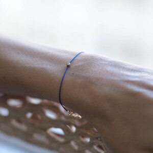 May include: A blue string bracelet with a small gold bead.