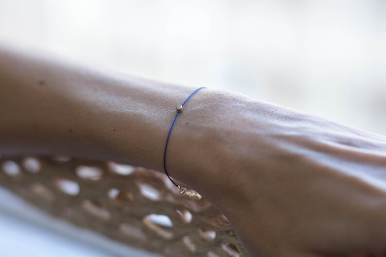 May include: A blue string bracelet with a small gold bead.