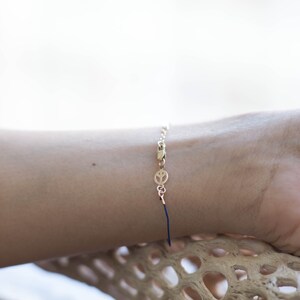 May include: A gold chain bracelet with a peace sign charm and a blue string tie closure.