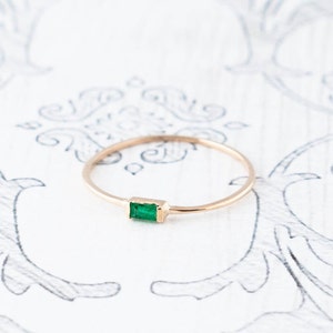 May include: A delicate gold ring with a single emerald green gemstone set in a rectangular shape.