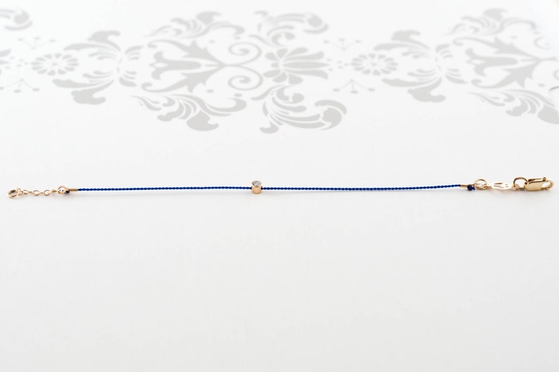 May include: A delicate blue string bracelet with a small gold bead featuring a tiny diamond.