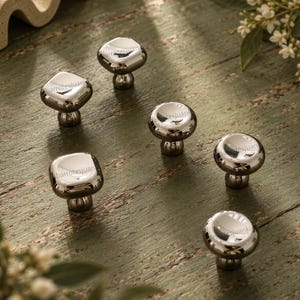 May include: A collection of six cabinet knobs with a polished chrome finish. Three knobs feature a square shape with rounded corners, while the other three knobs have a circular, mushroom-like design. Each knob includes a short, cylindrical base.