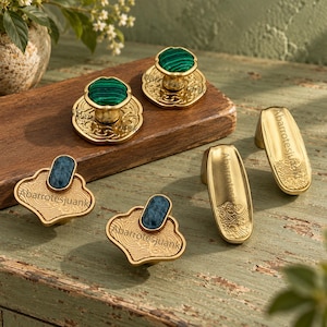 May include: A collection of gold-toned metal hardware including two round knobs with green malachite-style inlays, two cloud-shaped knobs with blue stone inlays, and two elongated handles. Each piece features the text Abarrotesjuank engraved.