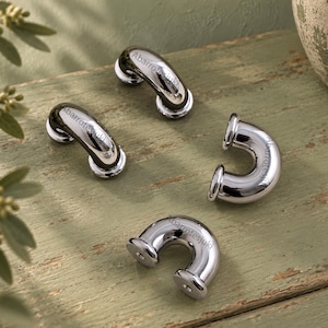 May include: Four polished chrome U-shaped cabinet pulls with a reflective metallic finish. Each piece features a curved handle design with circular mounting bases at both ends. The text Abarrotesjuki is printed on the surface of each handle.
