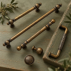 May include: A collection of antique brass cabinet hardware including three long bar pulls with rounded ends, one rectangular pull with a hammered texture, and two round knobs with a hammered finish. Each piece features the text Abarrotesjuanki.