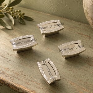 May include: Four rectangular cabinet knobs with a metallic silver finish, featuring a textured border and a smooth, recessed center. Each knob is marked with the text Abarrotesjuanki. The knobs are arranged in a scattered formation on a surface.