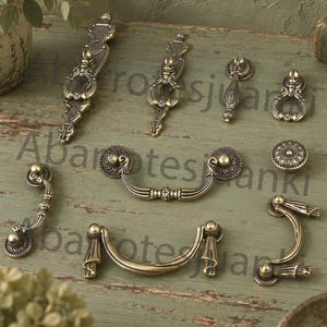 May include: A collection of antique brass-toned metal cabinet hardware including various drawer pulls, drop handles, and a circular knob. The pieces feature intricate embossed detailing, curved shapes, and a weathered finish with dark highlights.