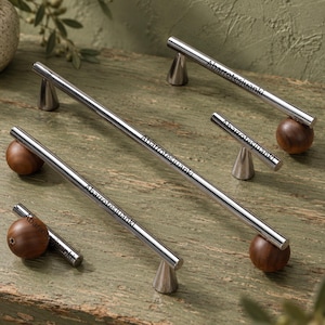 Può includere: Una collezione di maniglie per mobili composta da lunghe barre cilindriche in metallo argentato abbinate a basi rotonde in legno marrone scuro. Ogni barra argentata reca l'incisione Abarrotesjuanki. Il set include maniglie e pomelli di varie lunghezze.