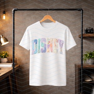 May include: A white short-sleeved t-shirt featuring the word DISNEY printed across the chest in a multi-colored, patterned block font. Each letter displays a unique design, including floral, plaid, and geometric prints in pastel shades.