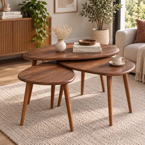 May include: A set of three nesting coffee tables made of dark brown wood with a smooth finish. Each table features a rounded, organic shape and three tapered legs. The tables are arranged in a tiered formation, showcasing the wood grain texture.