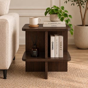 Op de afbeelding: Een donkerbruine houten bijzettafel met een ontwerp met twee niveaus, met een bovenoppervlak met een gespikkelde keramische mok en twee boeken getiteld The Kinfolk Home, en een onderste plank met een donkere glazen diffuser en drie boeken.