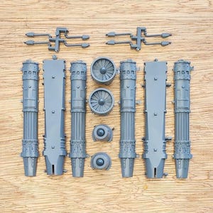 May include: A collection of grey plastic model kit parts including four long cylindrical engine components, two flat rectangular panels, two circular turbine fan pieces, two small conical caps, and two small dual-pronged connector pieces.