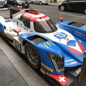 May include: A white, blue, and red endurance race car featuring the number 13, Vaillante Rebellion branding, and various sponsor logos including Motul, Dunlop, and McDonald's. The vehicle has a low-profile aerodynamic design with a rear wing.