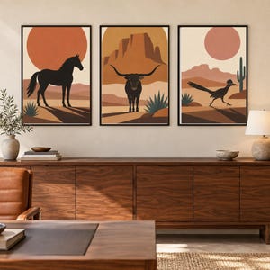 Peut inclure: Un ensemble de trois impressions d'art mural encadrées représentant des paysages désertiques avec un cheval noir, un bœuf longhorn et un géocoucou. Chaque impression affiche une palette de couleurs chaudes orange, marron et crème.