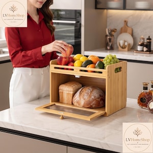 Peut inclure: Une boîte à pain en bambou à deux niveaux avec une porte abattante dotée d'un panneau en verre strié transparent. L'étagère supérieure contient divers fruits frais, dont des pommes rouges, des citrons jaunes, des oranges, du raisin et des avocats.