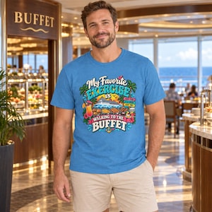 May include: A heather blue t-shirt featuring a colourful graphic print of a cruise ship, tropical drinks, and food trays with the text My Favorite EXERCISE IS WALKING TO THE BUFFET, GOOD FOOD, GOOD DRINKS, GOOD TIMES, and a small anchor icon.