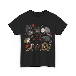 May include: A black short-sleeved t-shirt featuring a graphic print of various animals including a bat, spider, opossum, rat, toad, lizard, cockroach, and snake. The text "LOVE THE UNLOVED" is printed in red in the centre with small red star accents.