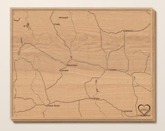 Peut inclure: Une plaque murale rectangulaire en bois brun clair présentant une carte gravée du Wyoming. La carte affiche les routes principales et les villes comme Powell, Cody, Riverton, Lander, Casper, Rawlins, Green River, Laramie et Cheyenne avec un cœur.