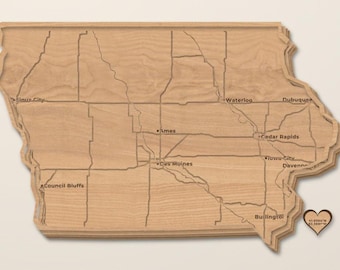 Peut inclure: Une carte en bois superposée de l'État de l'Iowa avec les noms des villes gravés, notamment Sioux City, Ames, Des Moines, Waterloo, Cedar Rapids, Iowa City, Davenport et Burlington. Une petite étiquette en bois en forme de cœur affiche des coordonnées.