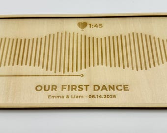 Peut inclure: Une plaque rectangulaire en bois clair avec un motif d'onde sonore gravé au laser. Le texte indique 1:45, 0:00, 3:30, OUR FIRST DANCE, et Emma & Liam 06.14.2026. Une petite icône en forme de cœur est placée au-dessus du graphique.