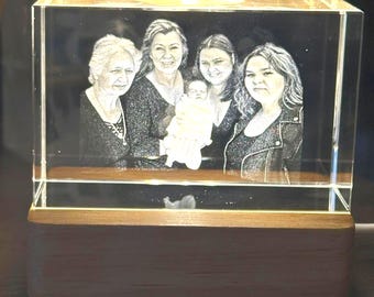 Peut inclure: Un bloc de verre rectangulaire présentant une image 3D gravée au laser de quatre adultes et d'un nourrisson. Le bloc de verre transparent est éclairé par le bas par une base en bois rectangulaire, mettant en valeur le portrait monochrome.
