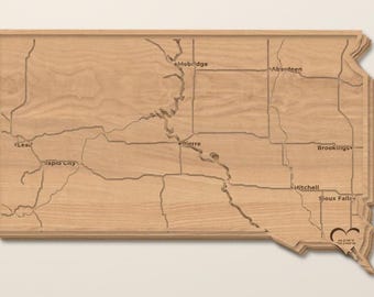 Peut inclure: Une carte murale en bois brun clair du Dakota du Sud avec des frontières d'État gravées, des rivières et des noms de villes comme Mobridge, Aberdeen, Lead, Rapid City, Pierre, Brookings, Mitchell et Sioux Falls, avec un cœur.